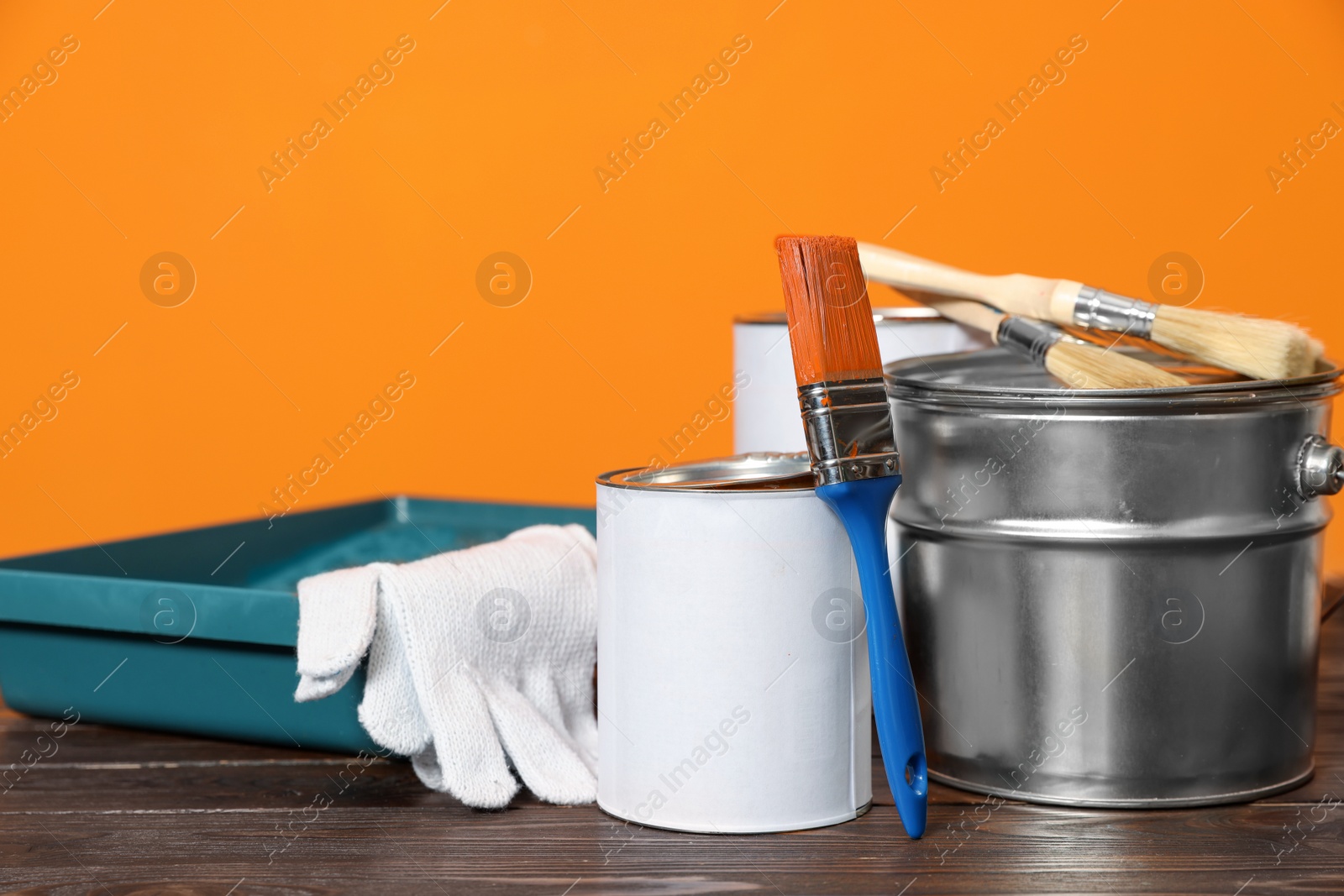 Photo of Can with paint, brush and renovation equipment on wooden table against orange background