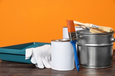 Photo of Can with paint, brush and renovation equipment on wooden table against orange background