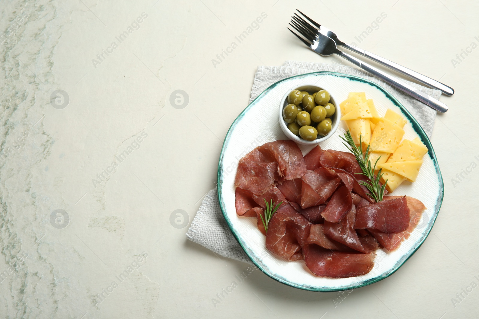 Photo of Delicious bresaola, cheese, olives and rosemary served on light textured table, top view. Space for text