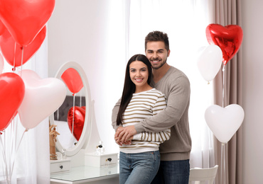 Photo of Lovely young couple in room decorated with heart shaped balloons. Valentine's day celebration