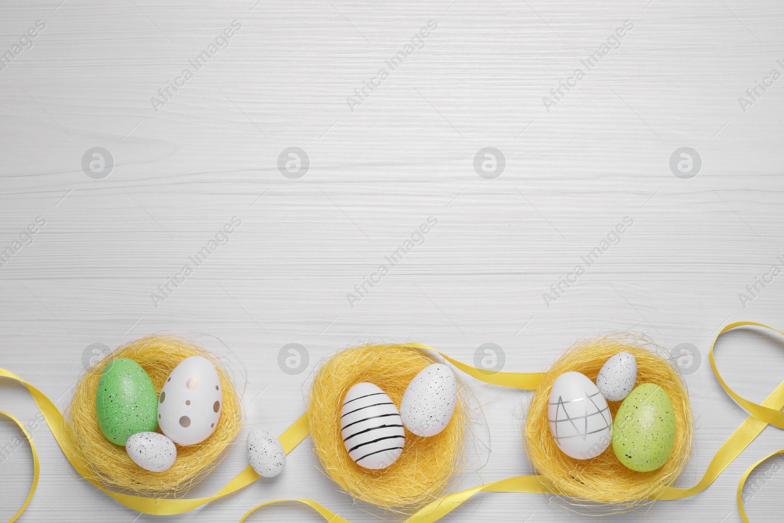 Photo of Flat lay composition with festively decorated Easter eggs on white wooden background. Space for text