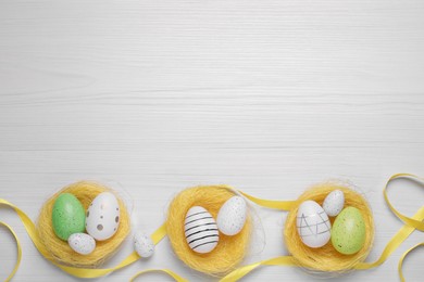 Flat lay composition with festively decorated Easter eggs on white wooden background. Space for text