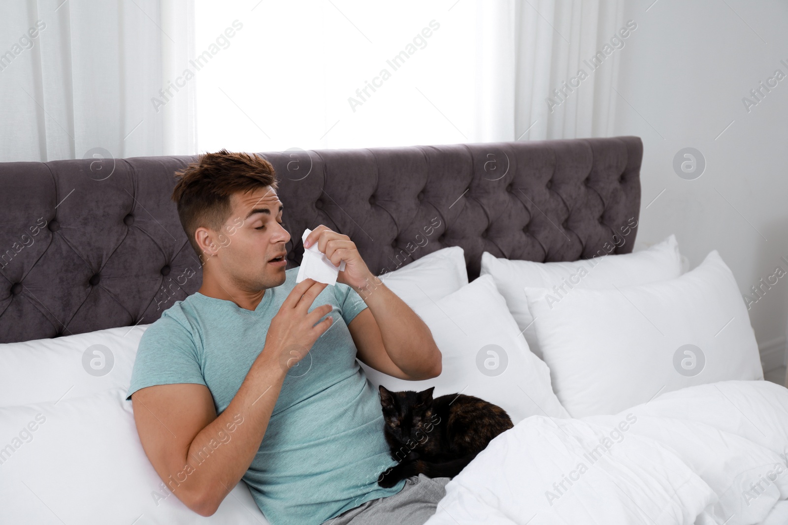 Photo of Young man with cat suffering from allergy in bedroom