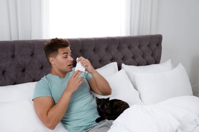 Young man with cat suffering from allergy in bedroom