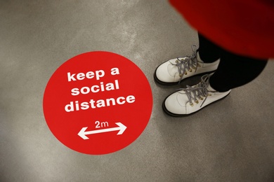 Image of Keep social distance as preventive measure during coronavirus outbreak. Red warning sign on floor in front of woman, closeup