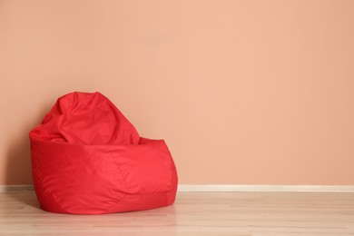 Photo of Red bean bag chair on floor near beige wall indoors, space for text