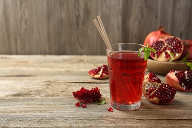 Photo of Tasty pomegranate juice in glass and fresh fruits on wooden table. Space for text