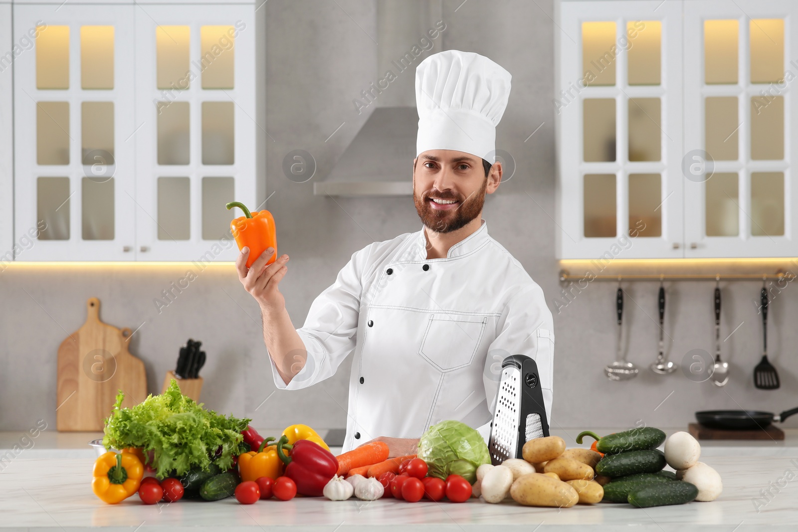 Photo of Portrait of professional chef with bell pepper near vegetables at marble table in kitchen