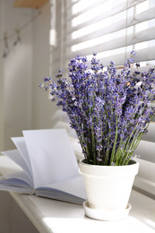 Photo of Beautiful lavender flowers and book on window sill indoors