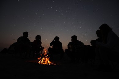 Photo of Group of friends gathering around bonfire in evening. Camping season