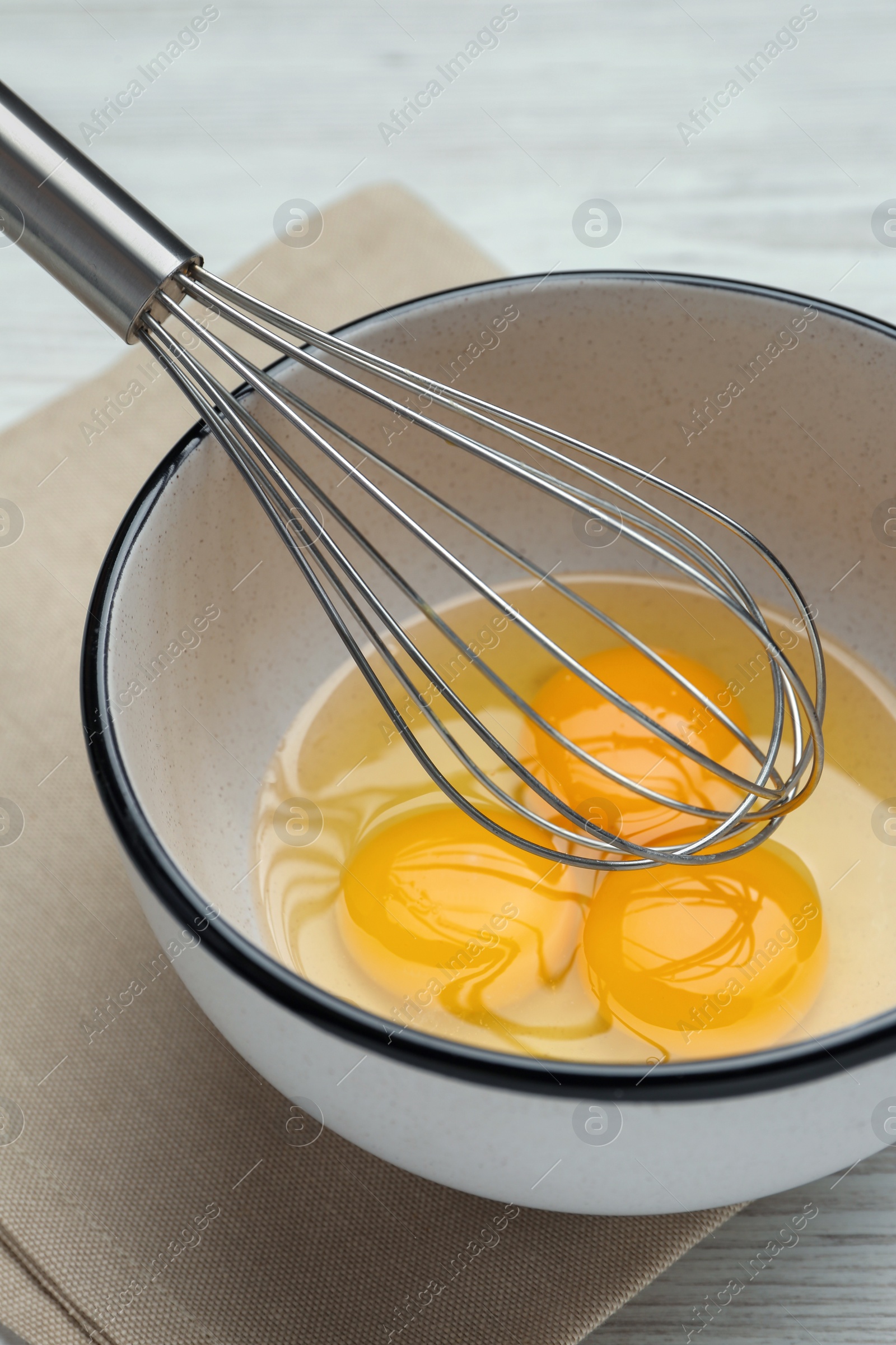 Photo of Whisk and eggs in bowl on white table, closeup