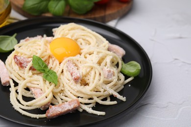 Photo of Plate of tasty pasta Carbonara with basil leaves and egg yolk on white textured table, closeup