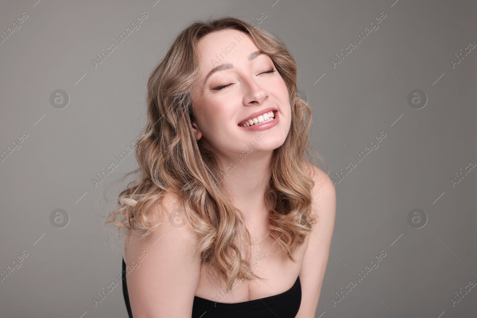 Photo of Portrait of smiling woman with curly hair on grey background