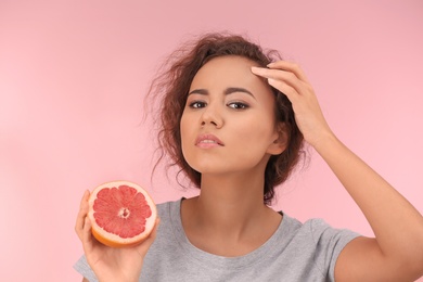 Photo of Beautiful young woman with acne problem holding grapefruit on color background. Skin allergy