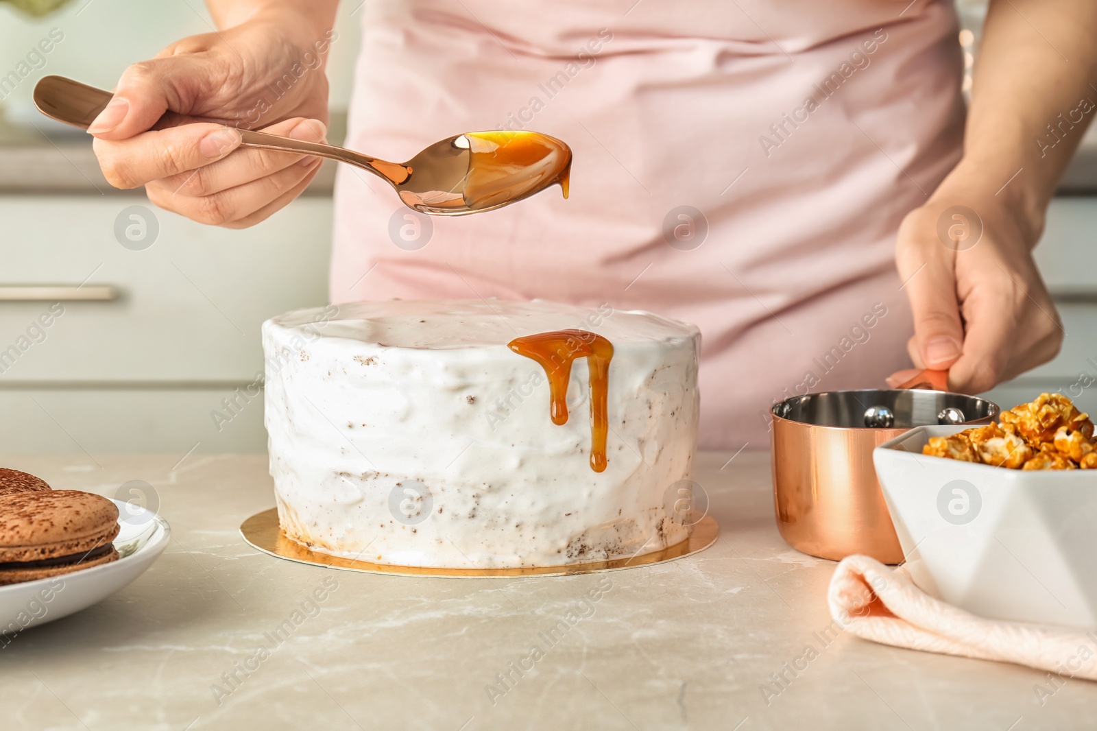 Photo of Young woman applying caramel sauce onto delicious homemade cake at table