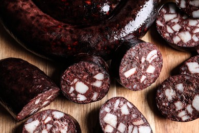 Cut tasty blood sausages on wooden background, flat lay