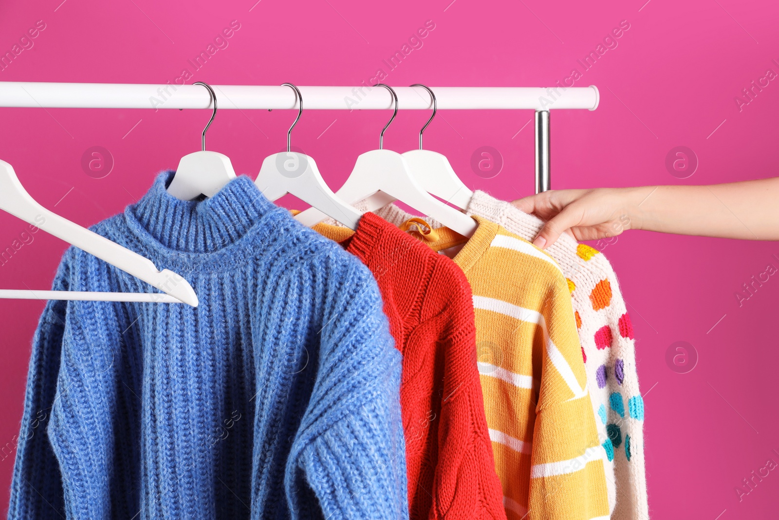 Photo of Woman choosing sweater on rack against color background