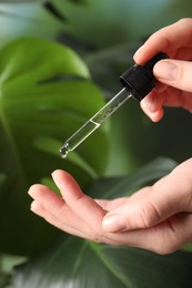 Photo of Woman applying cosmetic serum onto finger on green background, closeup