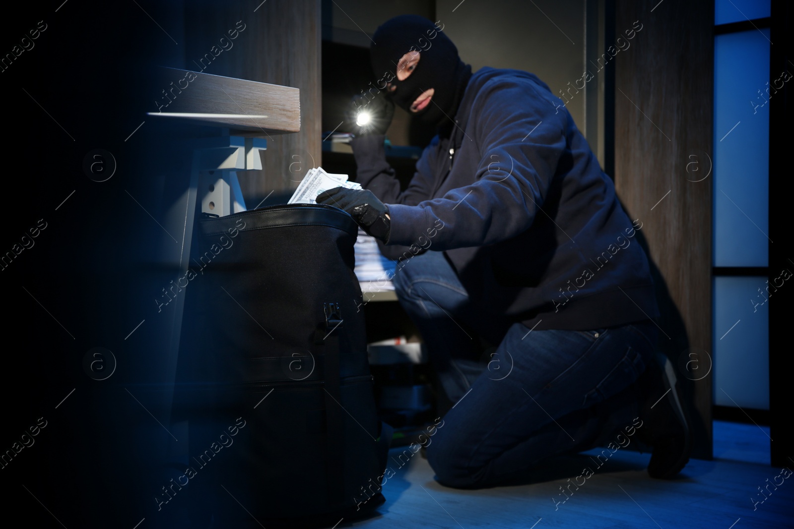 Photo of Thief taking money out of steel safe indoors at night