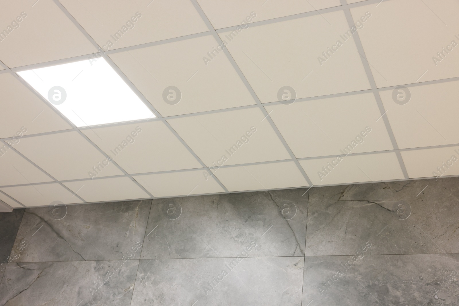 Photo of White ceiling with PVC tiles and lighting indoors, low angle view