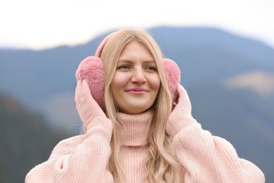 Photo of Young beautiful woman wearing warm earmuffs in mountains