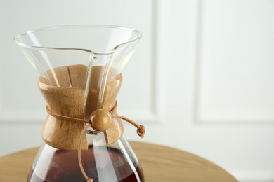 Photo of Glass chemex coffeemaker with coffee on table against white wall, closeup. Space for text