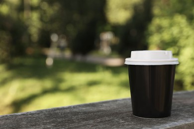 Takeaway paper cup with plastic lid on stone parapet outdoors, space for text