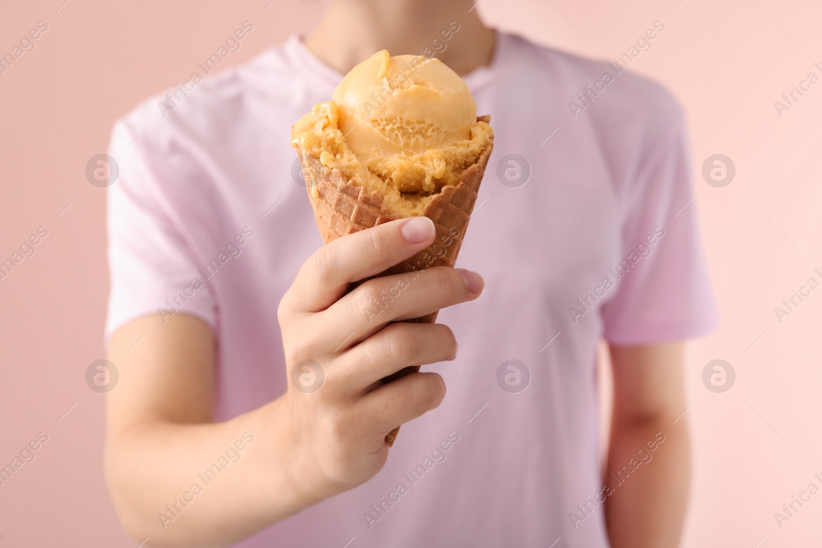 Photo of Woman holding yellow ice cream in wafer cone on pink background, closeup