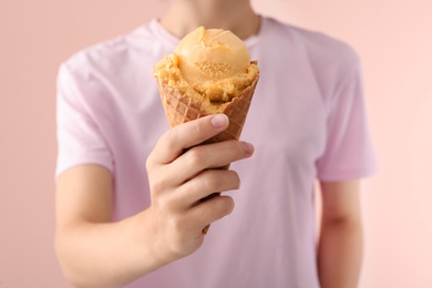 Photo of Woman holding yellow ice cream in wafer cone on pink background, closeup