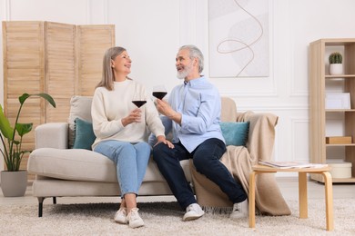Affectionate senior couple with glasses of wine on sofa indoors