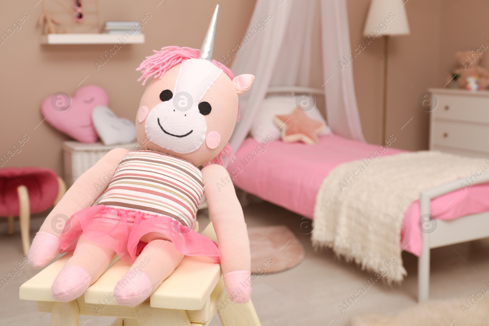 Photo of Soft toy unicorn on wooden stool in child's room, space for text. Interior design