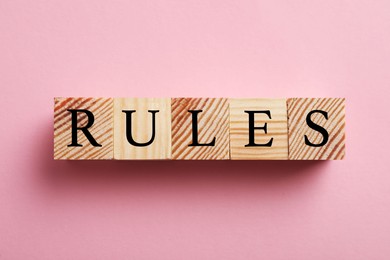 Photo of Word Rules made of wooden cubes with letters on pink background, flat lay