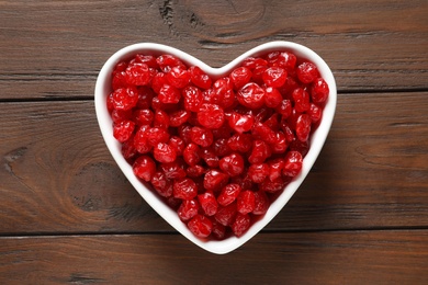 Photo of Heart shaped bowl of sweet cherries on wooden background, top view. Dried fruit as healthy snack
