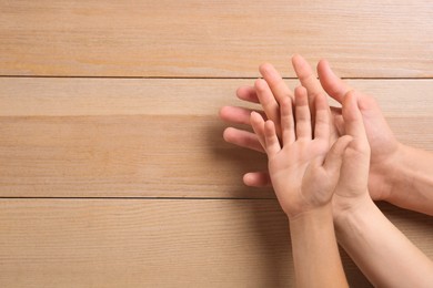 Family holding hands together on wooden background, top view. Space for text