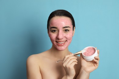 Woman applying pomegranate face mask on light blue background