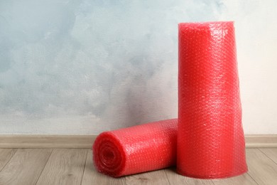 Photo of Red bubble wrap rolls on floor near light blue wall. Space for text