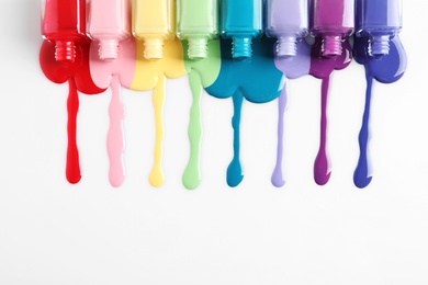 Spilled colorful nail polishes and bottles on white background, top view