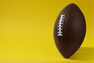 Photo of American football ball on yellow background, space for text