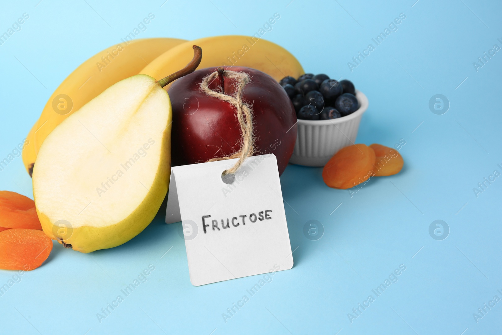 Photo of Card with word Fructose, delicious ripe fruits, blueberries and dried apricots on light blue background