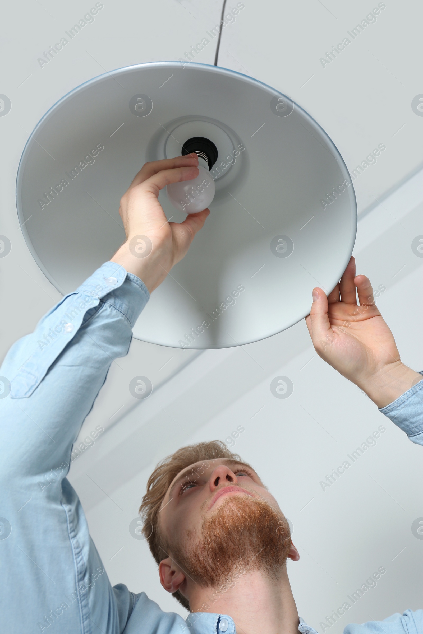 Photo of Man changing light bulb in pendant lamp indoors, low angle view