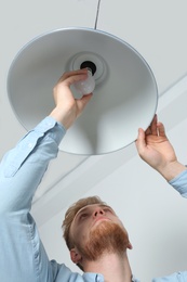 Photo of Man changing light bulb in pendant lamp indoors, low angle view