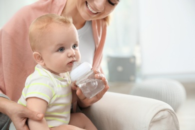 Photo of Lovely mother giving her baby drink from bottle in room