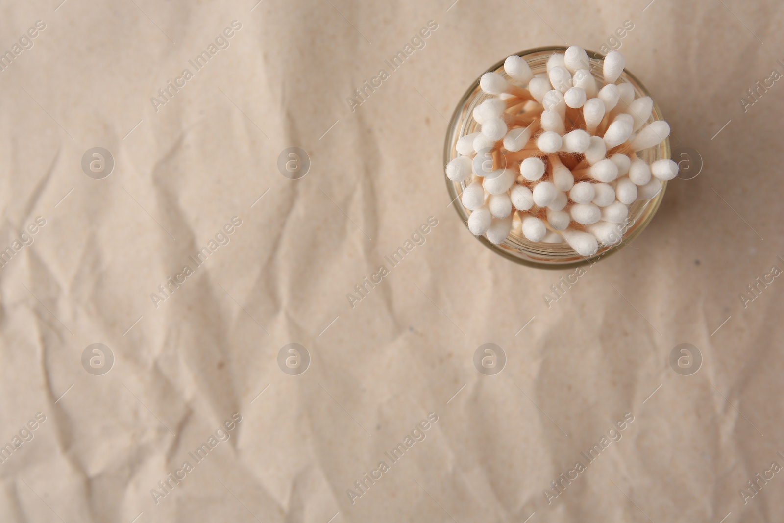 Photo of Jar of clean cotton buds on crumpled paper, top view. Space for text