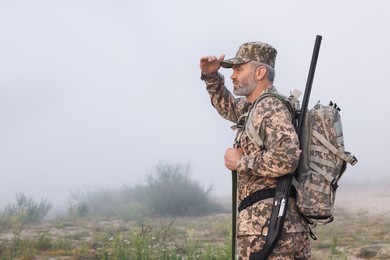 Man wearing camouflage with hunting rifle and backpack outdoors. Space for text