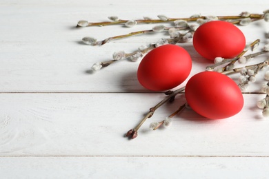 Photo of Red dyed Easter eggs and pussy willow on wooden table, space for text