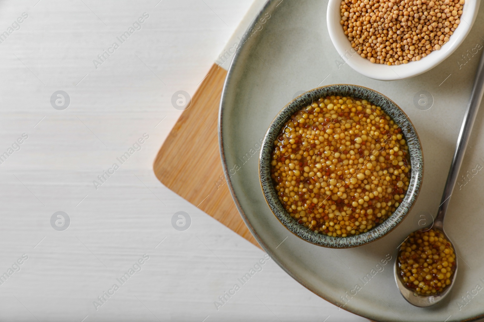 Photo of Bowl and spoon of whole grain mustard on white wooden table, flat lay. Space for text
