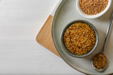 Bowl and spoon of whole grain mustard on white wooden table, flat lay. Space for text