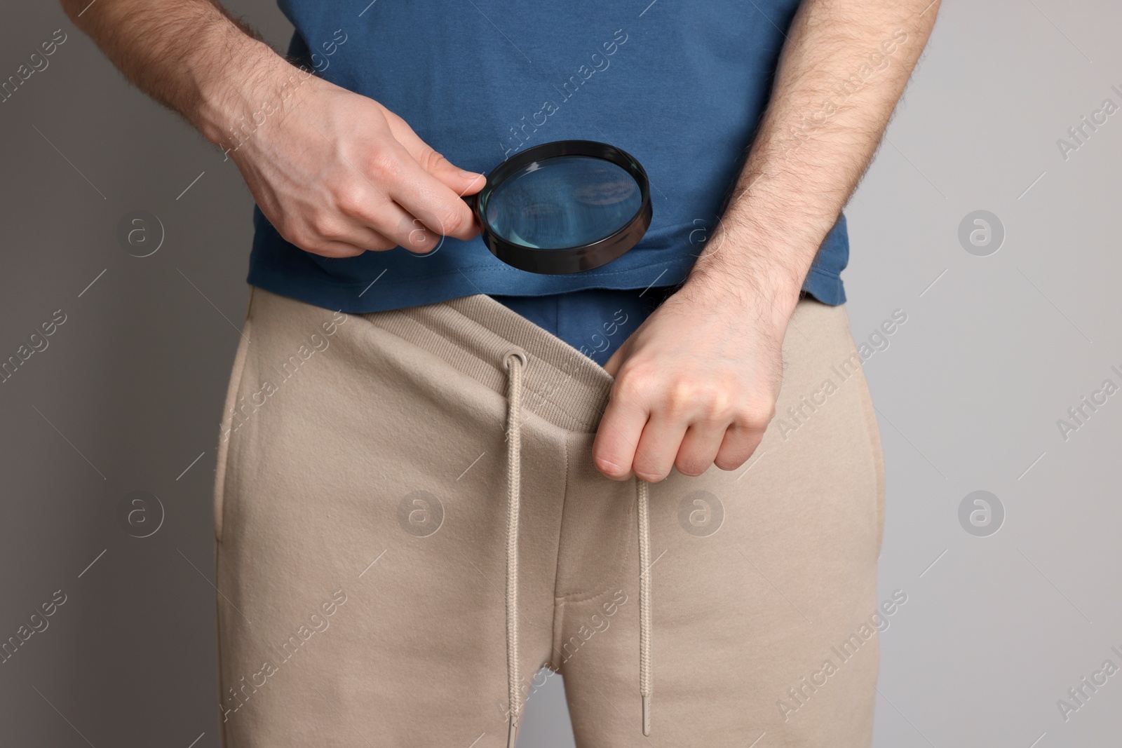 Photo of Man examining genital herpes with magnifying glass on beige background, closeup.