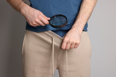 Man examining genital herpes with magnifying glass on beige background, closeup.