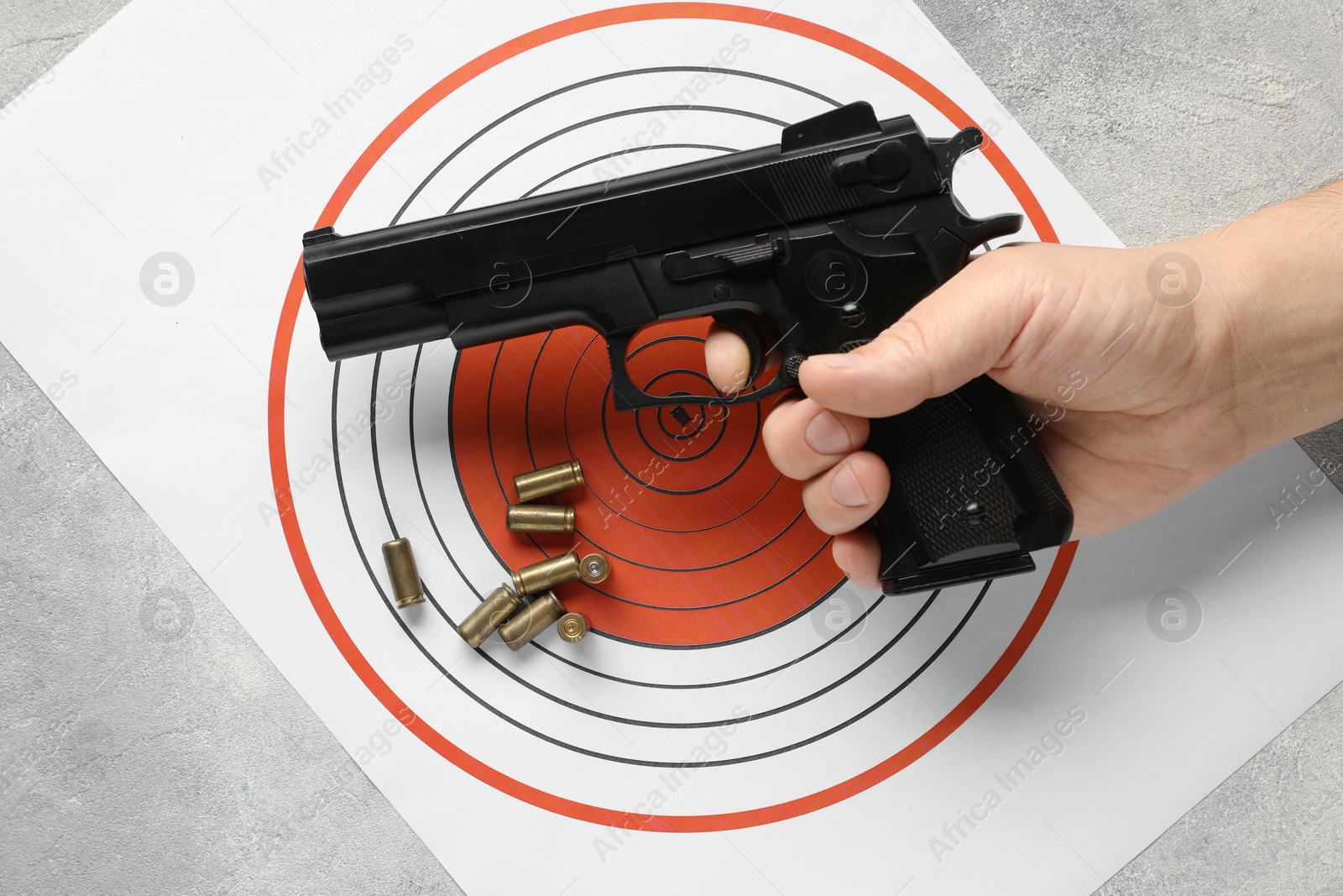 Photo of Man with handgun, shooting target and bullets at gray table, top view